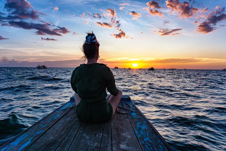 Girl sitting on a boat facing the river at sunset in the Floating Village in Siem Reap, Cambodia