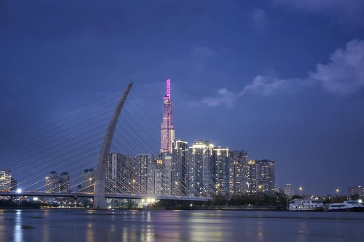 High tower in the background at night with pink lights on showcasing the riverside part of Ho Chi Mihn city