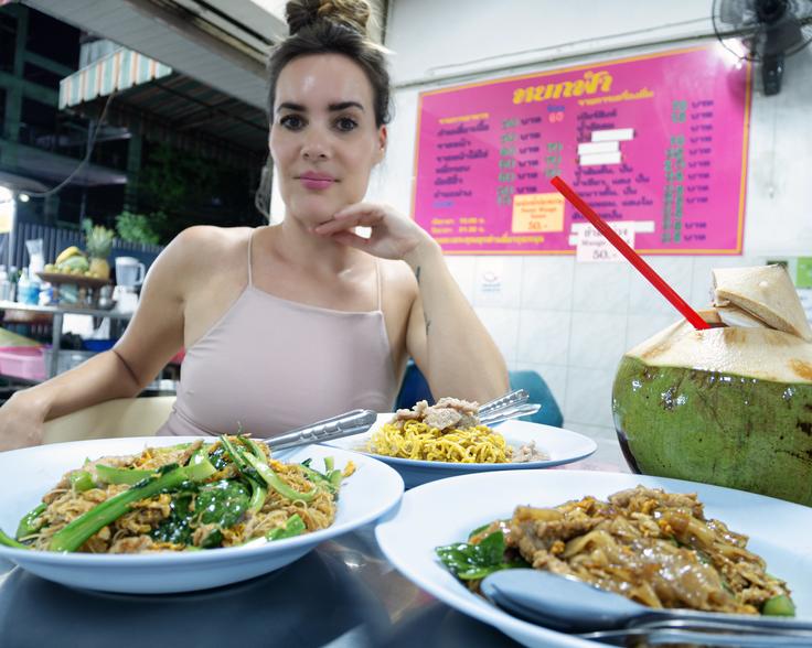 Girl eating three different Thai dishes of noodles stir fry with meat and vegetables