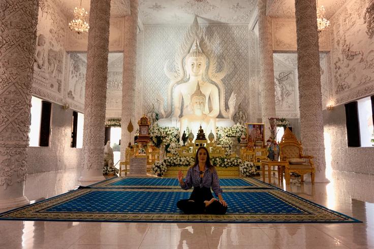 Girl sitting on the floor of a Thai temple praying to Buddha