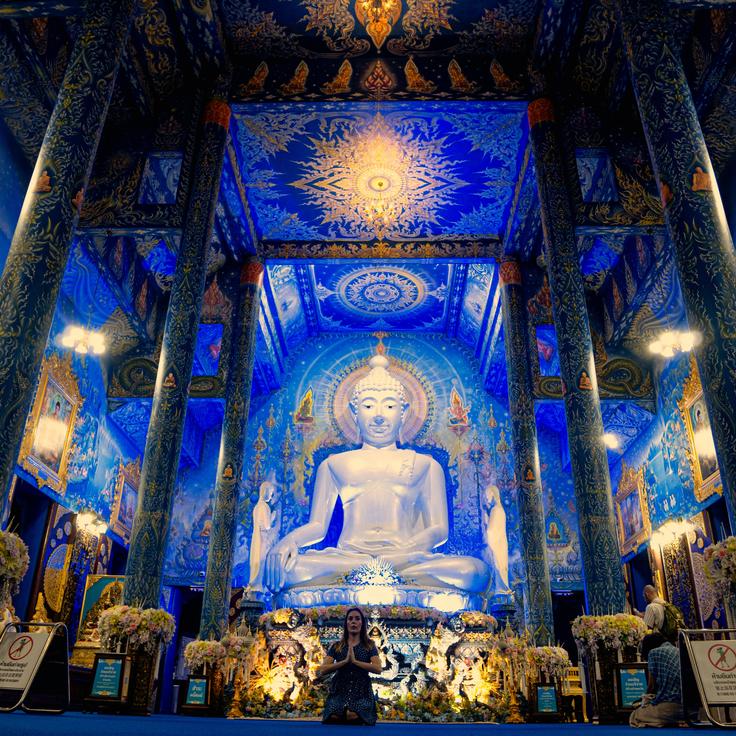 Girl sitting on the floor in the blue temple of Chiang Rai with Buddha behind her