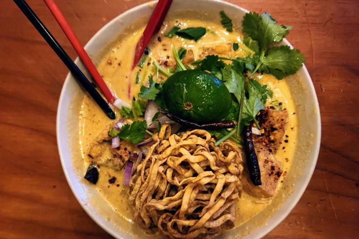 Shot of a colourful Khao Soi with toppings including crispy fried noodles, shallots, and pickled mustard greens