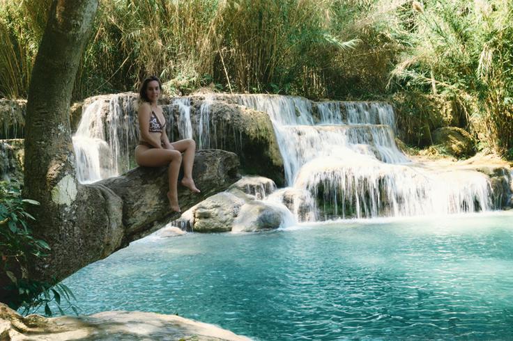 Shot of a girl sitting on a tree over the Kuang Si Falls in Luang Prabang