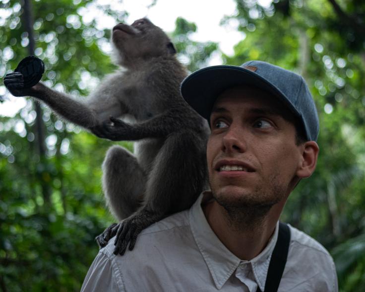 A person stands in Monkey Forest, Ubud, with a monkey perched on their shoulder, both enjoying the serenity of the natural surroundings