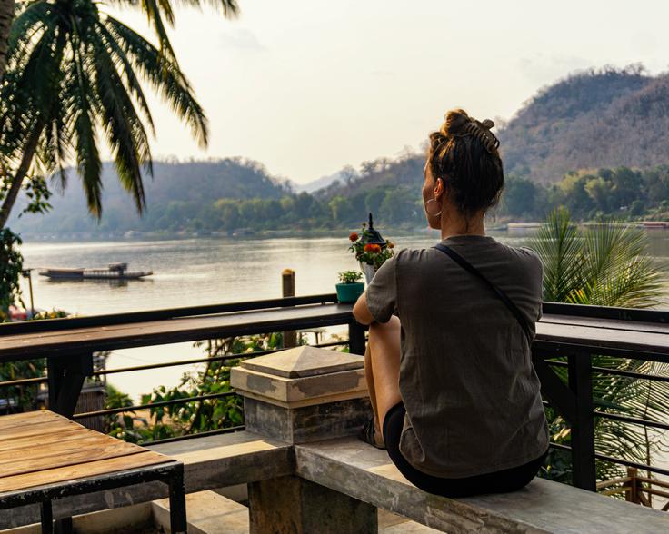 Girl sitting on a bench watching over the  Nam Khan river Luang Prabang at sunset