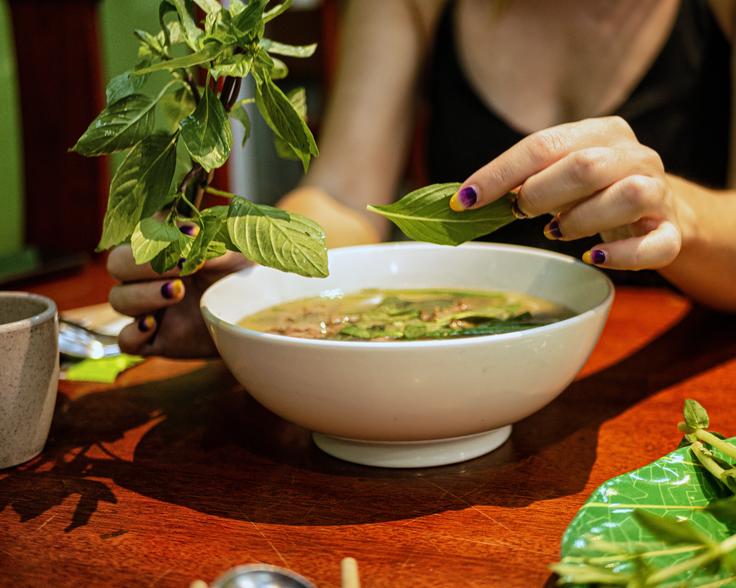 A bowl of Pho noodle soup with fresh leaves to be added to the soup