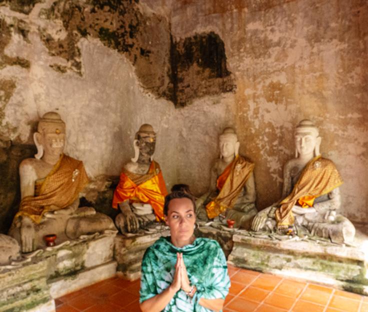 Shot of a girl in the cave next to rock praying monks at Wat Pha Lat temple